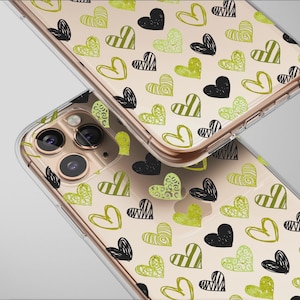 May include: Two clear phone cases with a gold-colored frame. The cases are decorated with a pattern of black, green, and yellow hearts. The hearts have various designs, including stripes and doodles. The phone cases are on a light gray background.