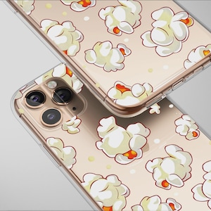 Puede incluir: Dos fundas transparentes para teléfono con un diseño de palomitas de maíz. Las fundas tienen un fondo beige claro con un patrón repetido de granos de palomitas de maíz blancos y naranjas. Las fundas están en ángulo, mostrando las lentes de la cámara y los bordes del teléfono.