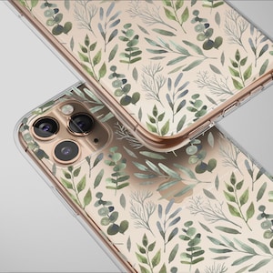 May include: Two clear phone cases with a botanical design. The cases feature a pattern of green and gray leaves and branches on a beige background. The cases have gold-colored edges and are angled towards the viewer.