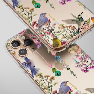 Puede incluir: Dos fundas transparentes para teléfono con un diseño floral y de pájaros. Las fundas presentan un fondo beige con ilustraciones de pájaros coloridos, flores rosas y amarillas y follaje verde. Las fundas tienen un borde dorado.