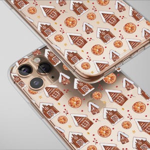 May include: Two clear phone cases with a repeating pattern of gingerbread houses, orange slices, and red berries on a beige background. The cases have a gold-colored border and are angled towards the viewer.