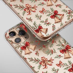 Puede incluir: Dos fundas transparentes para teléfono con un diseño navideño festivo. Las fundas presentan un patrón repetido de campanas doradas, lazos rojos, ramitas verdes y bayas rojas sobre un fondo crema. Las fundas están en ángulo.