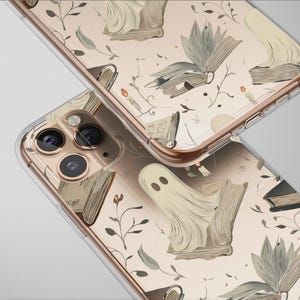 Puede incluir: Dos fundas transparentes para teléfono con un patrón repetido de fantasmas, libros, velas y elementos botánicos en tonos beige y gris. Las fundas tienen un marco dorado.