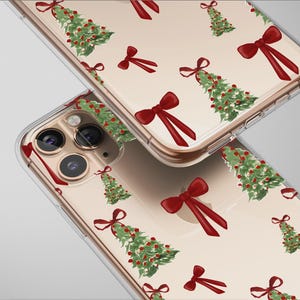 May include: Two clear phone cases featuring a repeating pattern of green Christmas trees and red bows. The cases are angled, displaying the design. The cases have a gold-coloured trim.