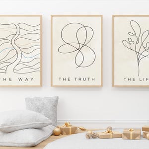 May include: Three framed art prints with minimalist line drawings and text: "THE WAY," "THE TRUTH," and "THE LIFE." The prints are in light wood frames. The scene includes a Christmas tree, wrapped gifts, and decorative pillows.