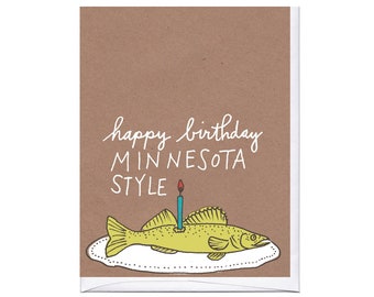 May include: A brown card with the text "happy birthday MINNESOTA STYLE" and a drawing of a yellow fish with a lit candle on top of it.