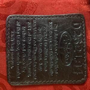 May include: A dark brown leather rectangular patch with rounded corners, embossed with the Brighton logo and text, stitched onto a vibrant red fabric lining featuring a repeating tonal pattern. The text reads: The Brighton Collection. Handbags are individually crafted in China from quality leather. Any markings on the surface are part of the natural beauty, texture and character of the leather, which make each bag unique.