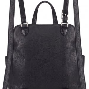 May include: A black backpack with a textured surface, featuring two adjustable shoulder straps with silver-toned metal buckles and hardware, a top carry handle, and a square-shaped main compartment with a zipper closure at the top.