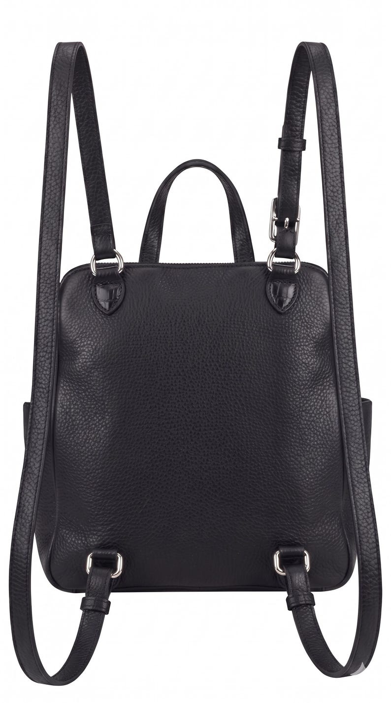 May include: A black backpack with a textured surface, featuring two adjustable shoulder straps with silver-toned metal buckles and hardware, a top carry handle, and a square-shaped main compartment with a zipper closure at the top.
