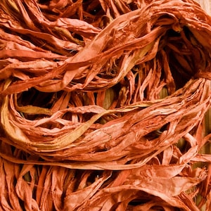 May include: Close-up of a bundle of orange-red silk ribbon. The ribbon is loosely woven and has a slightly frayed texture. The ribbons are tied together in a bundle, suitable for crafting or decorative purposes.