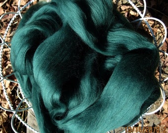 May include: A deep green pile of wool roving in a white metal basket. The wool is soft and fluffy, and it is perfect for spinning or felting.