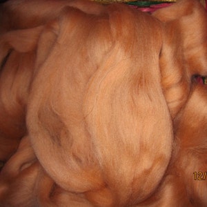May include: A close-up of a pile of soft, light orange wool fiber. The wool is fluffy and appears to be spun.