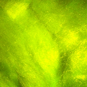 May include: Close-up of a vibrant, textured material in shades of green and yellow. The fibers appear soft and slightly translucent, creating a luminous effect. The overall texture is dense with a subtle, organic pattern.