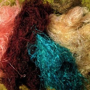 May include: A collection of colorful, fluffy yarn fibers in shades of pink, brown, teal, and cream. The fibers are loose and tangled, creating a textured and visually appealing display.