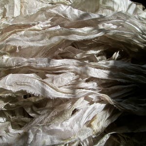 May include: A pile of white silk ribbon with a slightly frayed texture. The ribbon is arranged in a loose, flowing pattern, creating a soft and delicate look.