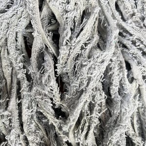 May include: Close-up of a gray mop head with a textured, frayed design. The mop head is made of multiple strands of fabric, creating a dense, absorbent surface. The color is a muted gray.