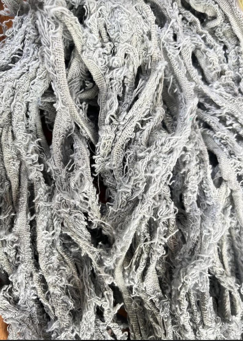 May include: Close-up of a gray mop head with a textured, frayed design. The mop head is made of multiple strands of fabric, creating a dense, absorbent surface. The color is a muted gray.