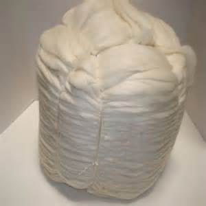 May include: A large bundle of white wool roving, tightly packed and secured with a string. The wool appears soft and fluffy, with visible layers and folds. The overall shape is cylindrical, suggesting it's ready for spinning or other textile projects.