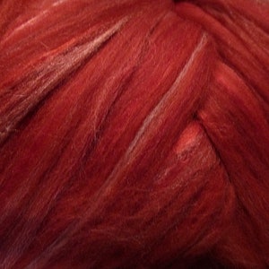 May include: Close-up of a red and white wool roving. The roving is arranged in a braided pattern, showing the texture of the fibers.