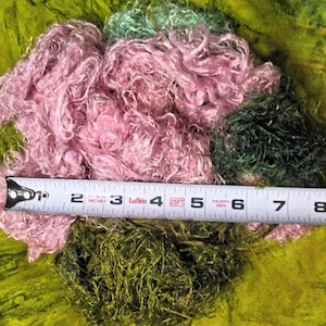 May include: A close-up of a pile of pink and green fiber with a tape measure laying across the top. The tape measure reads 1 to 8 inches.