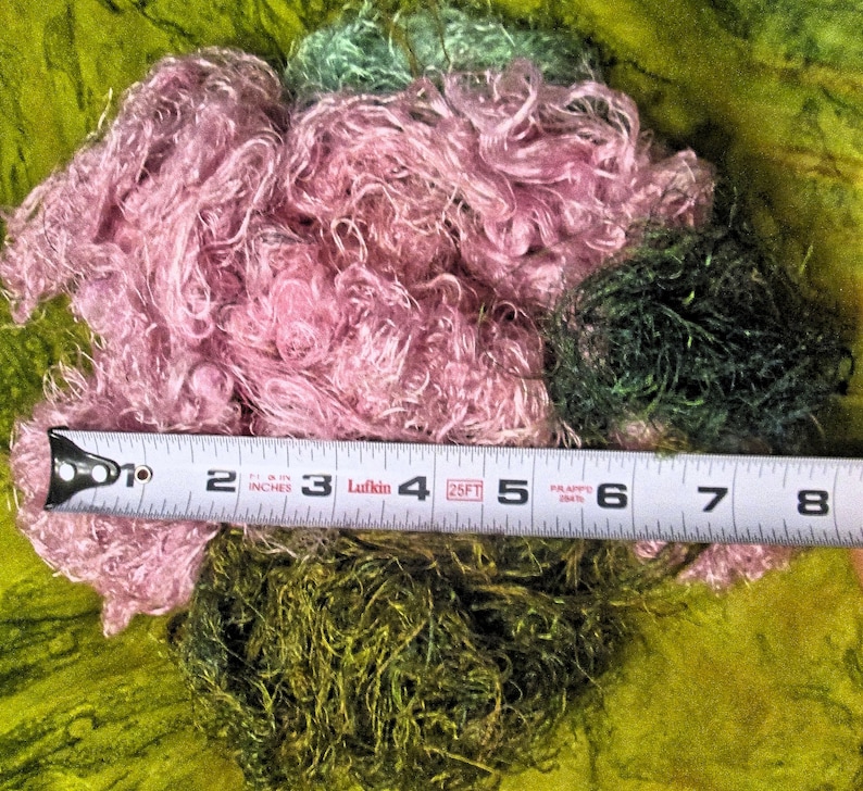 May include: A close-up of a pile of pink and green fiber with a tape measure laying across the top. The tape measure reads 1 to 8 inches.