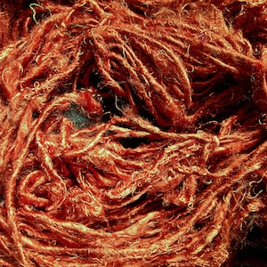 May include: Close-up of a tangled mass of reddish-brown yarn. The yarn appears to be made of natural fibers, with a slightly textured and uneven surface. The strands are tightly packed together, creating a dense and intricate pattern. Ideal for crafting projects.