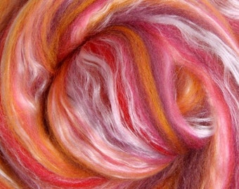 May include: Close-up of a swirl of colourful fibre. The fibre is a blend of red, pink, orange, and white, creating a vibrant and textured appearance. The fibres are soft and fluffy, ideal for crafting projects.