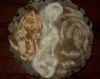 May include: Three piles of silk fibers in a ceramic bowl. The fibers are white, light beige, and a deeper beige color.