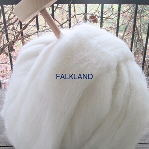 May include: A large ball of white wool with a wooden spindle inserted in the top. The text "FALKLAND" is printed in blue on the wool. The wool appears soft and fluffy, suitable for spinning or crafting.