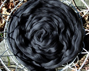 May include: A close-up of a large, black, fluffy ball of yarn in a white wire basket. The yarn is tightly wound in a spiral shape.