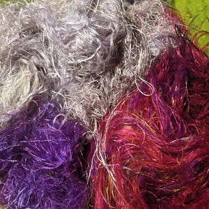 May include: A pile of colorful yarn in shades of purple, pink, and gray. The yarn is soft and fluffy, and it would be perfect for knitting or crocheting.