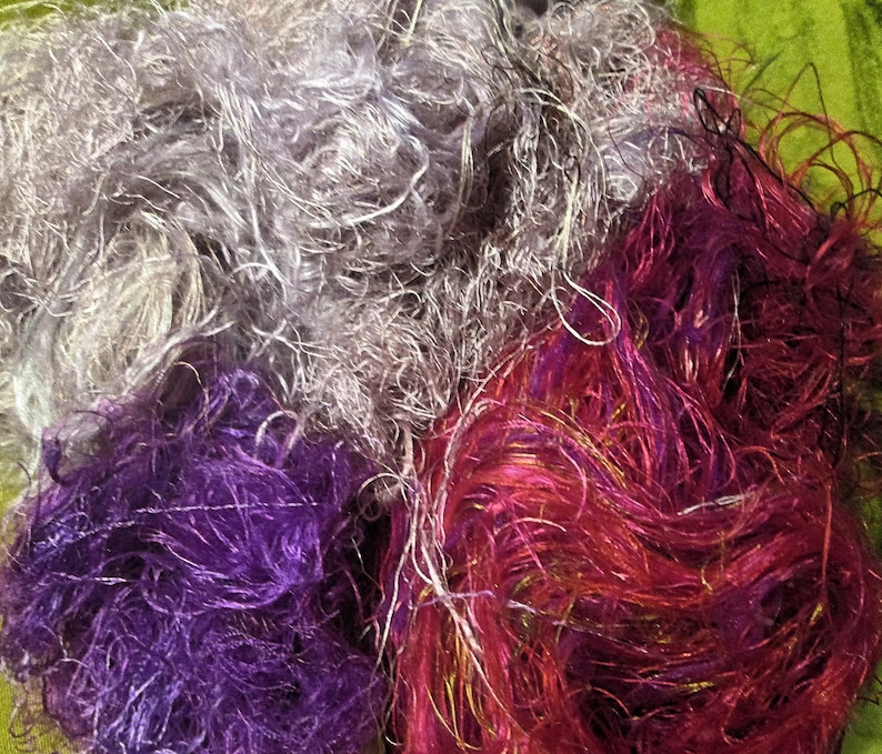 May include: A pile of colorful yarn in shades of purple, pink, and gray. The yarn is soft and fluffy, and it would be perfect for knitting or crocheting.