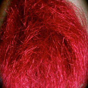 May include: A close-up of a bundle of bright red metallic fibers. The fibers are long and thin, and they are arranged in a random pattern. The fibers are shiny and reflect light.