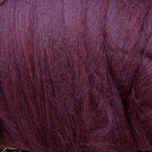 May include: Close-up of a mass of deep burgundy-colored wool roving. The fibers are soft and fluffy, with a slightly textured appearance. This wool is suitable for various fiber art projects, including felting and spinning.
