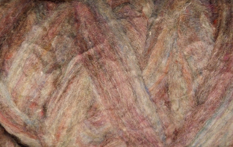 May include: Close-up of a bundle of colorful wool fibers in shades of brown, pink, and blue. The fibers are soft and fluffy, and they are arranged in a random pattern.