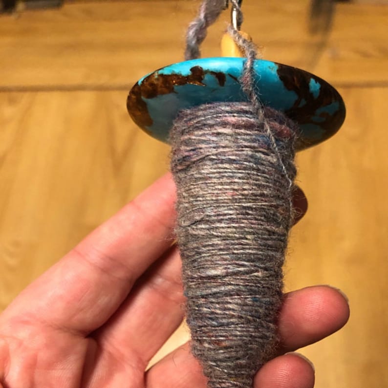 May include: A spinning wheel with a turquoise and brown whorl and a gray yarn bobbin.