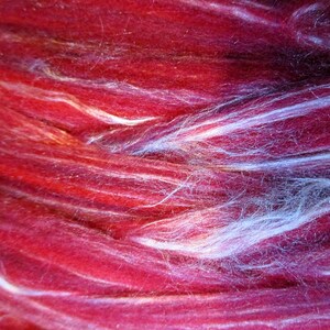 May include: Close-up of a red and white yarn with a soft, fuzzy texture. The yarn is arranged in a swirling pattern, creating a sense of movement and depth.
