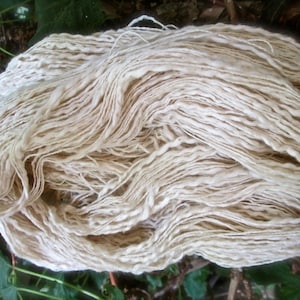 May include: A large bundle of undyed, natural-colored yarn. The yarn appears to be thick and textured, with a slightly irregular appearance. The fibers are loosely spun, creating a soft, inviting look. Ideal for knitting, crocheting, or other fiber arts projects.
