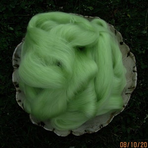 May include: A large pile of light green wool fiber in a white ceramic bowl. The wool is soft and fluffy, and it is perfect for spinning or felting.