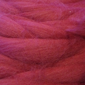 May include: Close-up of a bundle of vibrant, deep red merino wool roving. The fibers are soft and fluffy, with a slight sheen, ideal for various fiber art projects like felting and spinning. The wool is a rich, saturated color.