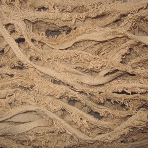 May include: A pile of tan, frayed fabric strips. The fabric is woven and has a rough texture.