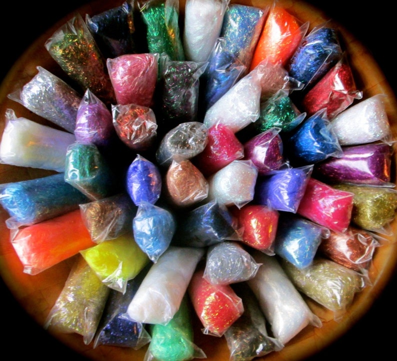 May include: Assortment of colorful glitter in individual clear plastic bags. The glitter is arranged in a circle on a wooden surface.