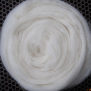 May include: A close-up of a white, fluffy, circular ball of wool fiber. The wool is tightly packed and has a soft, natural texture.