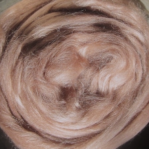 May include: A close-up of a light pink, fluffy, and soft fiber. The fiber is arranged in a circular pattern, creating a swirling effect.