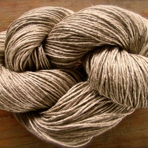May include: A close-up of a skein of natural brown linen yarn. The yarn is twisted and knotted, creating a textured and rustic look.