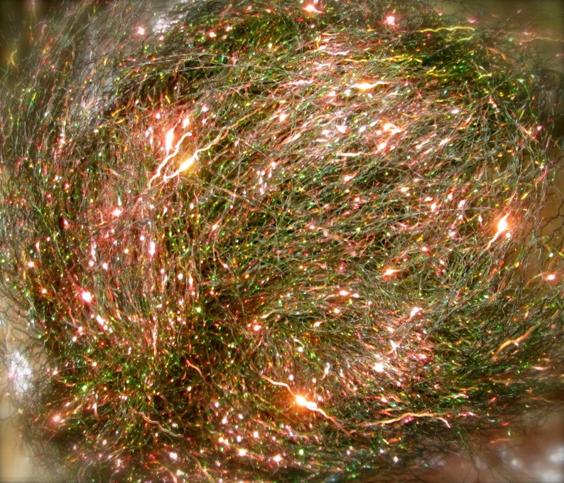 May include: A close-up of a bundle of iridescent green, pink, and gold holographic craft thread. The thread is very fine and has a sparkly, shimmering appearance.