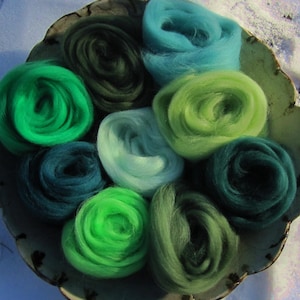 May include: A collection of nine different shades of green and blue wool roving, arranged in a circle on a white surface. The wool is soft and fluffy, and the colors are vibrant and beautiful.