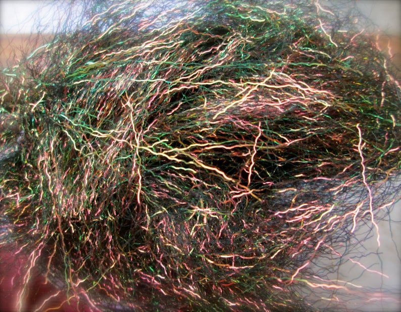May include: A close-up of a bundle of iridescent fly tying material. The material is a mix of black, green, and pink fibers with a holographic sheen.