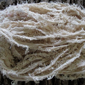 May include: A pile of off-white, frayed fabric strips. The fabric is loosely woven and has a natural, rustic look.