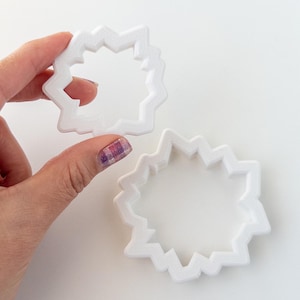 May include: Two white plastic cookie cutters shaped like a starburst. The cutters are different sizes.